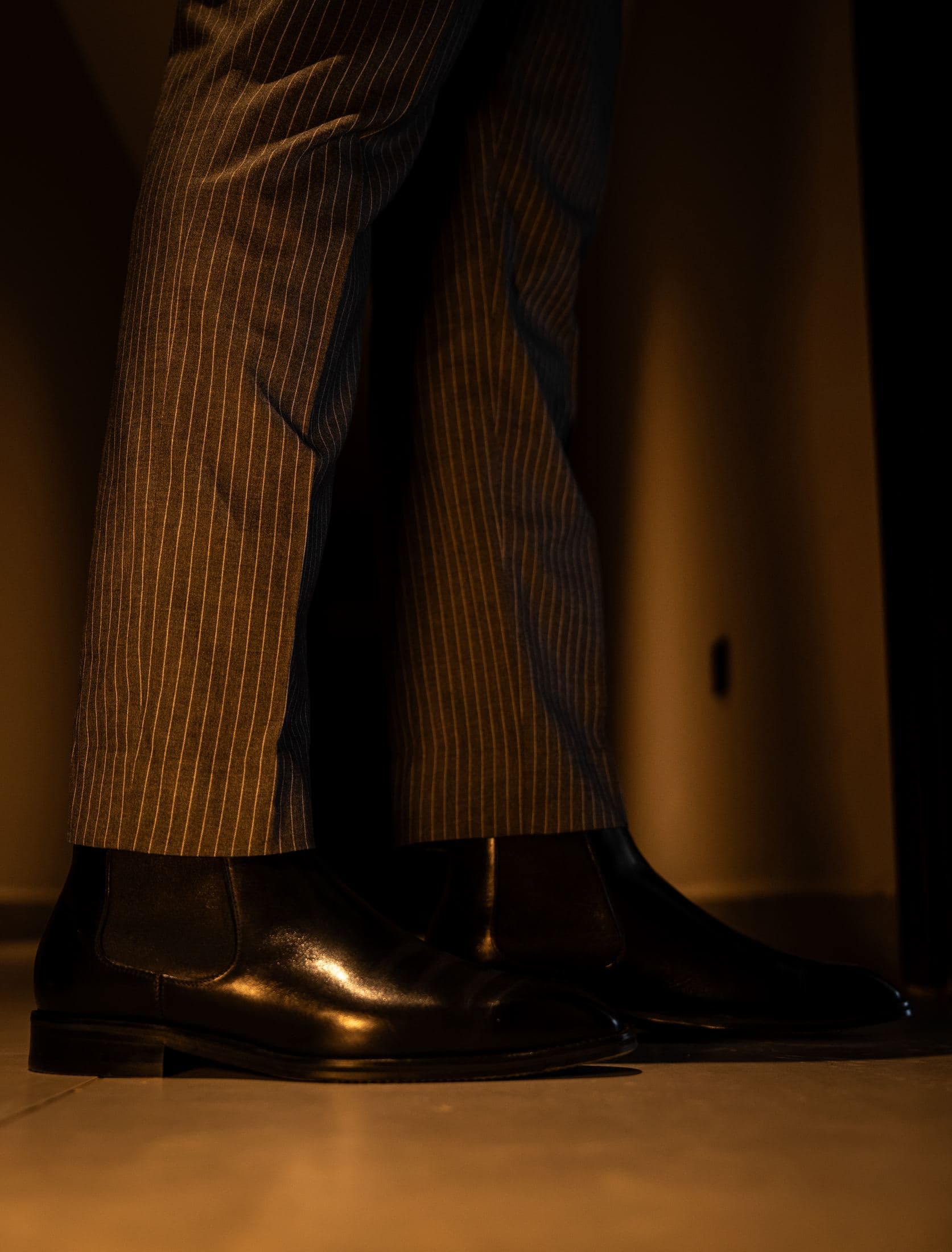 A man standing in pinstripe trousers and polished black shoes