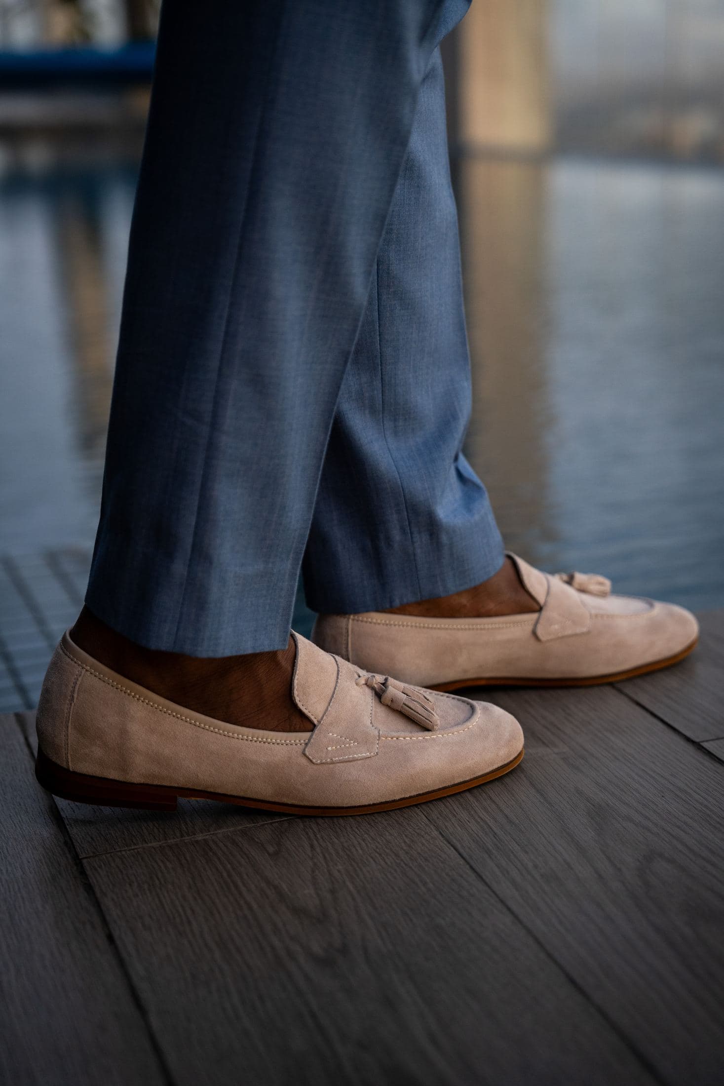 Stone suede tassel loafers on a deck above the water at golden hour